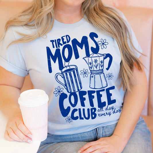 Person wearing a t-shirt with 'Tired Moms Coffee Club' design, holding a coffee cup.