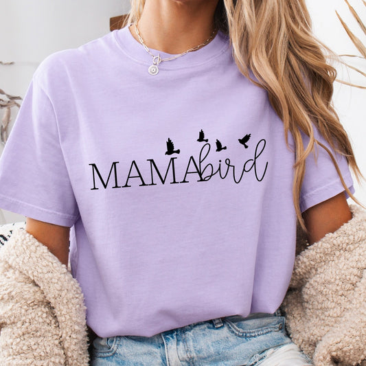 Person wearing a purple 'MAMAbird' t-shirt with denim shorts in a cozy indoor setting.