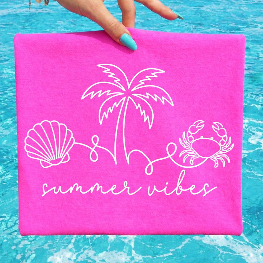 Pink towel with beach-themed designs and 'summer vibes' text held over blue water.