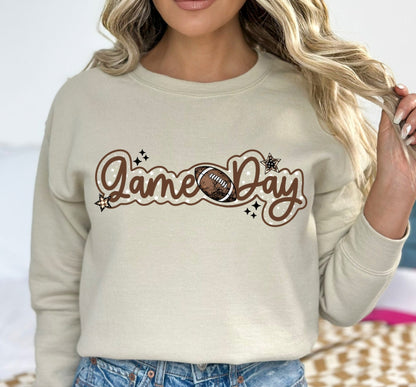 Person wearing a beige sweatshirt with 'Game Day' and football graphic.