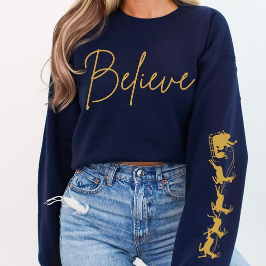 Person wearing a navy sweatshirt with 'Believe' in gold and a graphic design, paired with blue jeans.