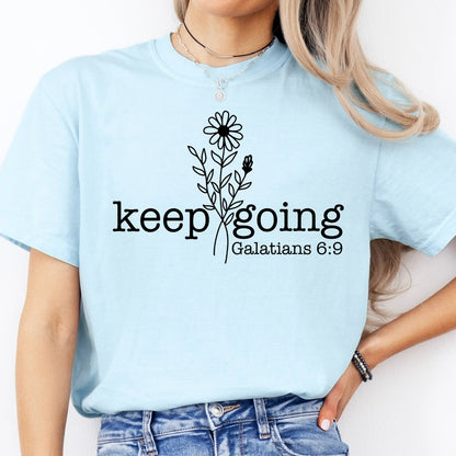 Person wearing a light blue t-shirt with 'keep going Galatians 6:9' text and floral design.