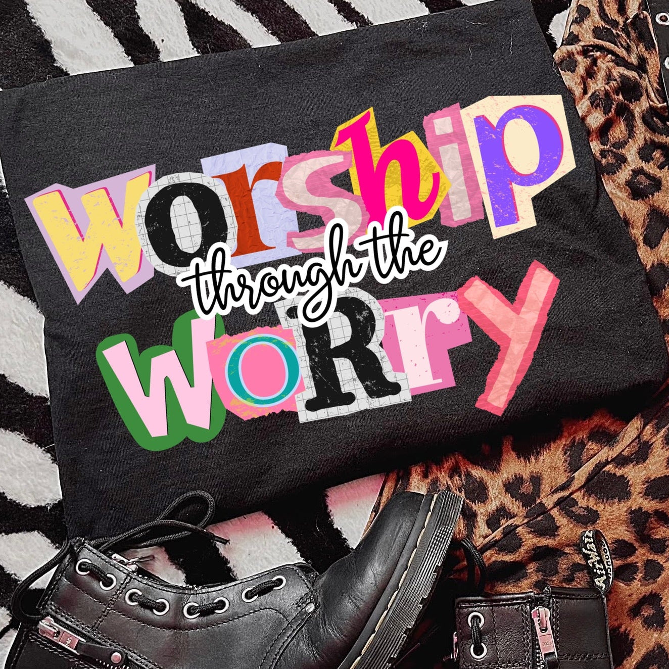 Black t-shirt with colorful text 'Worship through the Worry' on a patterned surface with shoes.