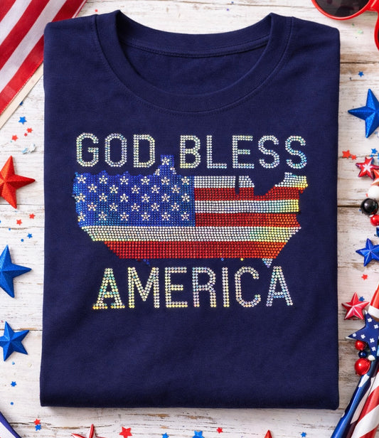 Navy blue t-shirt with 'God Bless America' text and American flag design on a wooden surface with festive decorations.