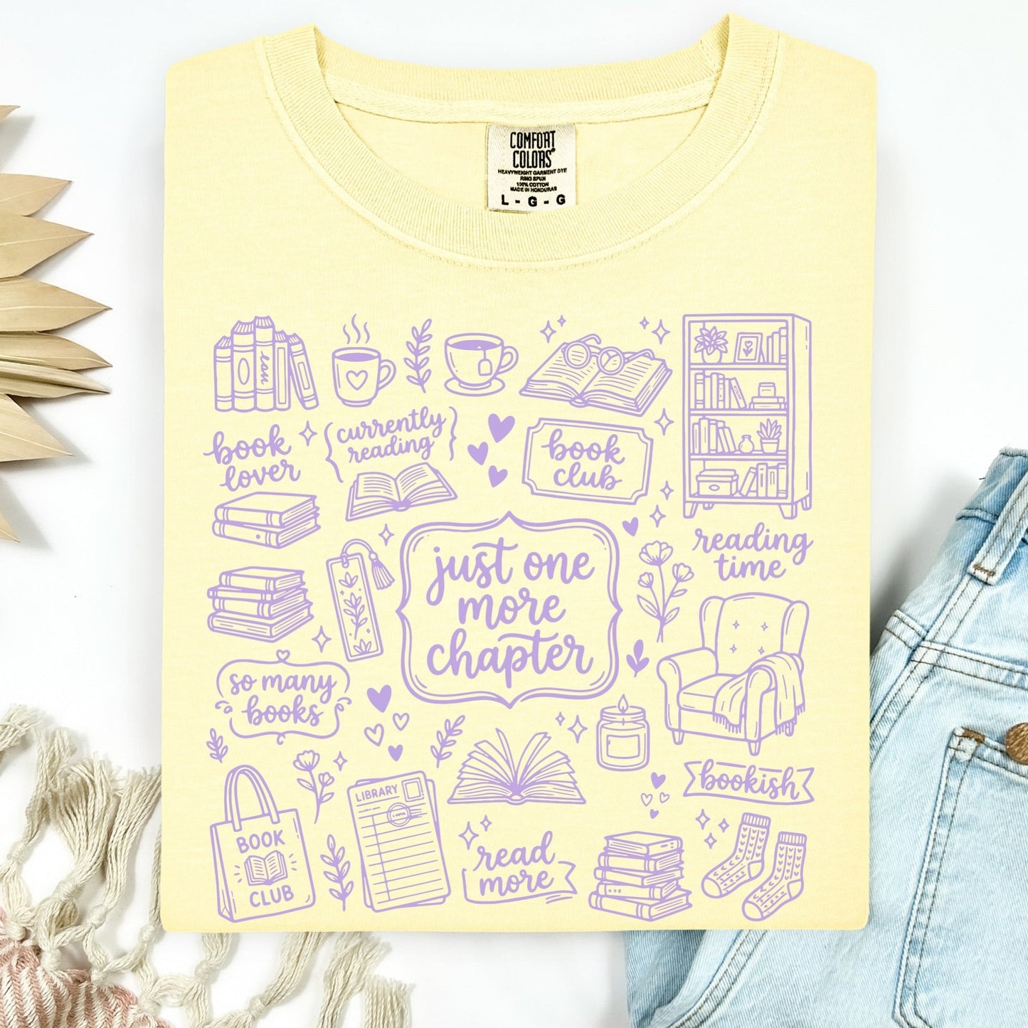 Yellow t-shirt with purple book-themed graphics and text on a white background