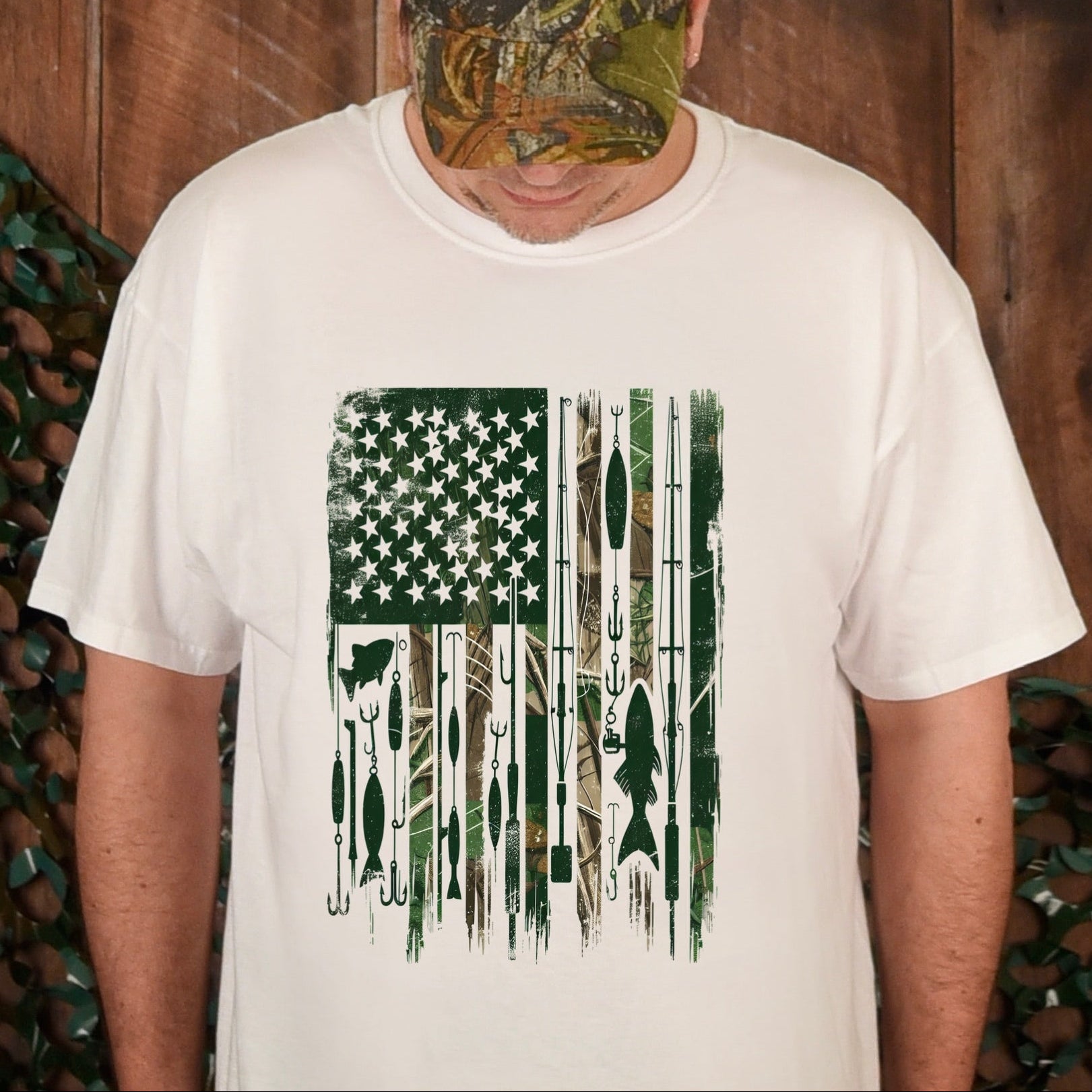 Person wearing a white t-shirt with a graphic design and a camouflage cap, standing against a wooden background.