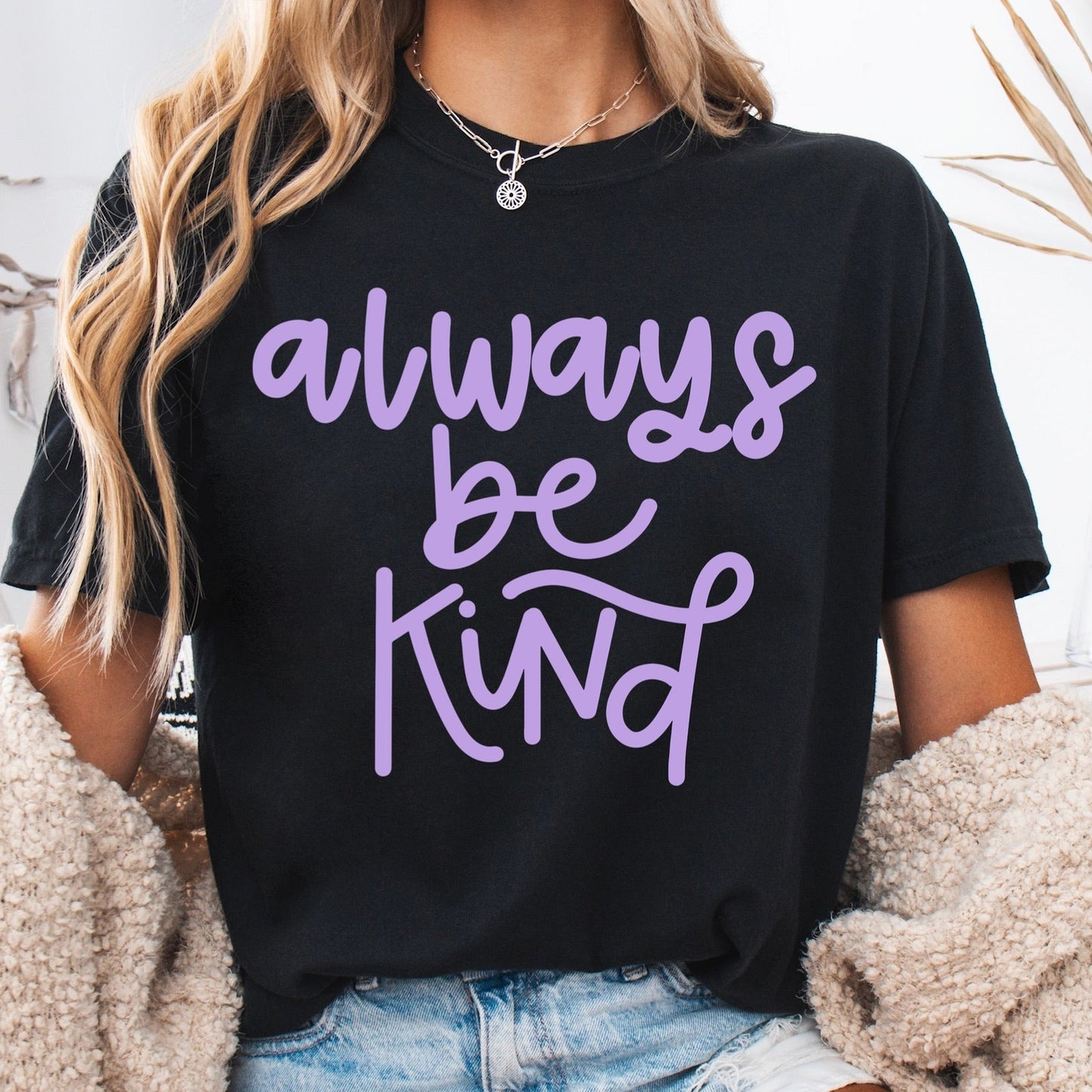 Person wearing a black t-shirt with 'always be kind' text in purple, sitting on a couch.