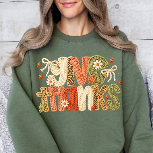 Person wearing a green sweatshirt with 'Give Thanks' embroidery sitting on a white couch.