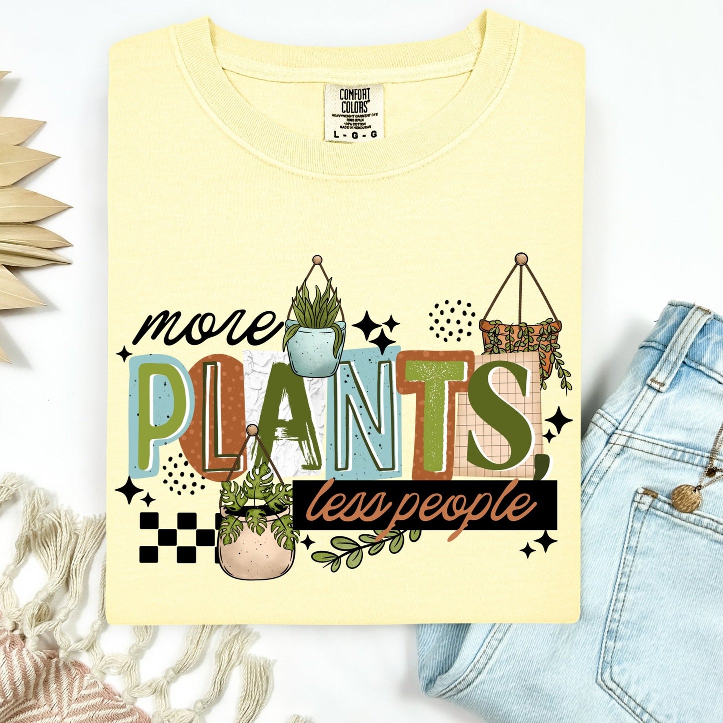 Yellow t-shirt with 'more plants less people' text and plant graphics on a white background.