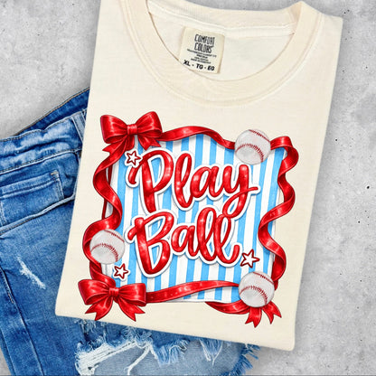 Folded t-shirt with 'Play Ball' design on a concrete surface