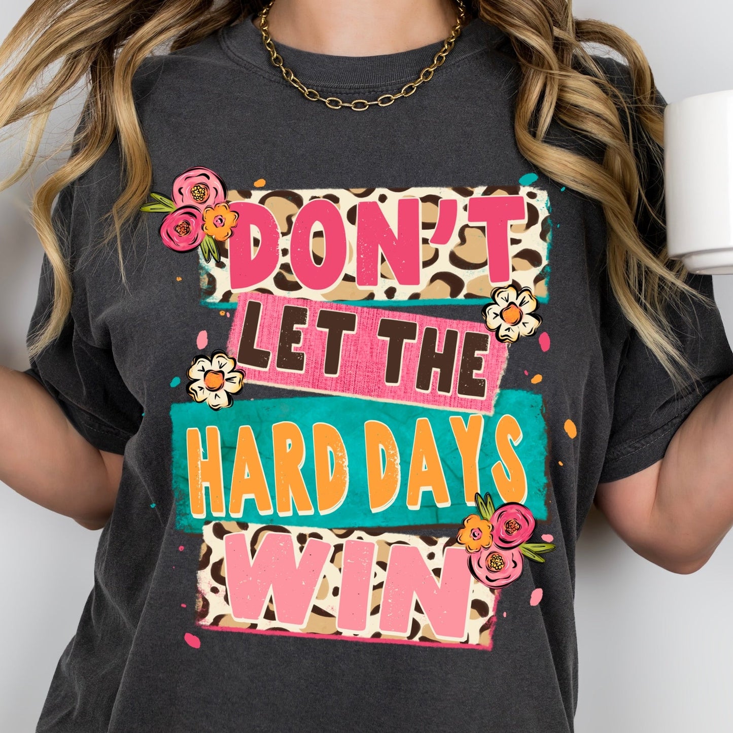 Person wearing a black t-shirt with colorful text and graphics, holding a white mug.