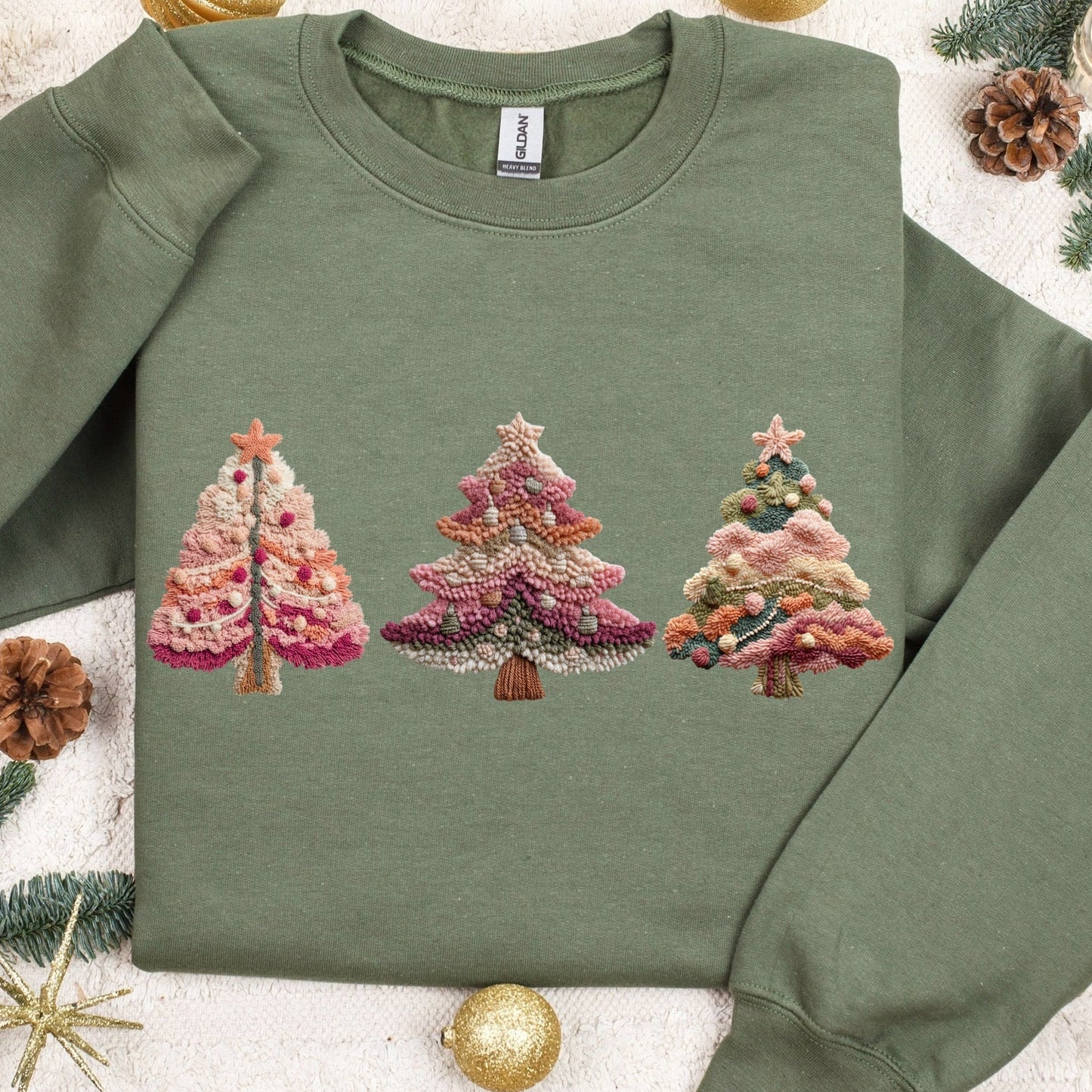 Green sweatshirt with embroidered Christmas tree design on a decorative background with ornaments and pine branches.
