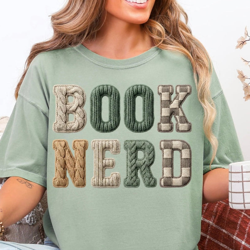 Woman wearing a green 'BOOK NERD' t-shirt, sitting on a couch with a mug.