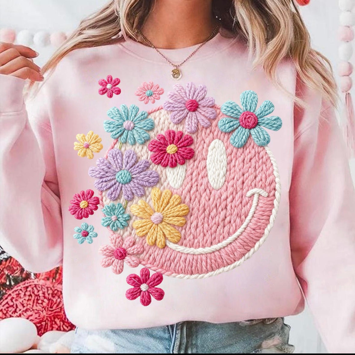 Pink sweatshirt with colorful floral designs and a smiley face on a white background