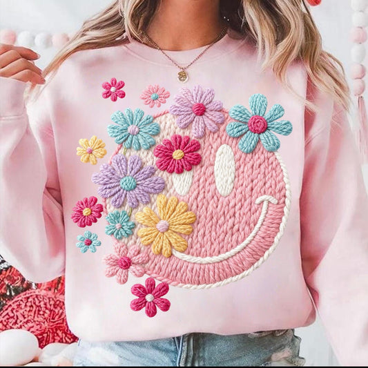 Pink sweatshirt with colorful floral designs and a smiley face on a white background