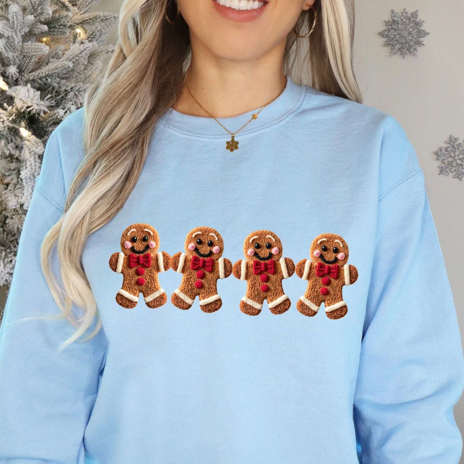 Person wearing a light blue sweatshirt with gingerbread man design in front of a Christmas tree.
