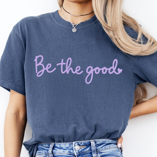 Person wearing a blue t-shirt with 'Be the good' text and blue jeans on a white background