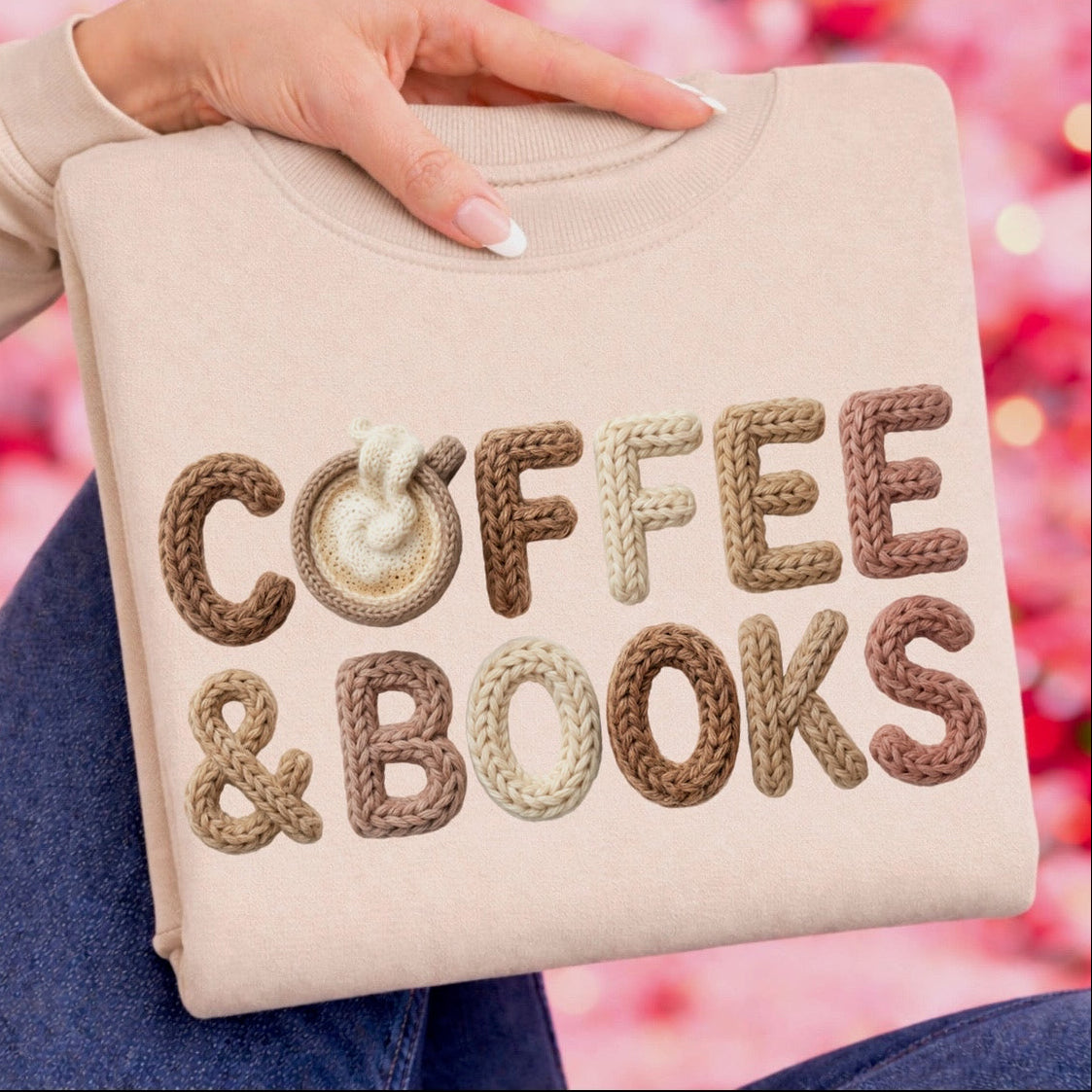 Beige pillow with 'COFFEE & BOOKS' text in brown and beige embroidery held by a person against a blurred pink background.
