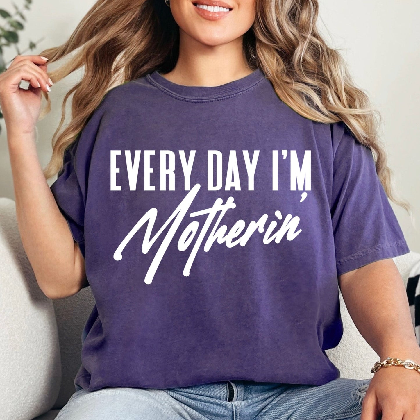 Person wearing a purple t-shirt with 'Every Day I'm Motherin' text, sitting on a couch.