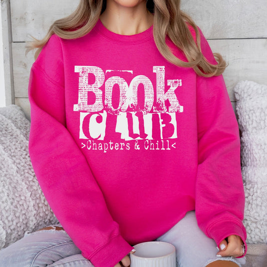 Person wearing a pink sweatshirt with 'Book Club > Chapters & Chill' text, sitting on a couch.