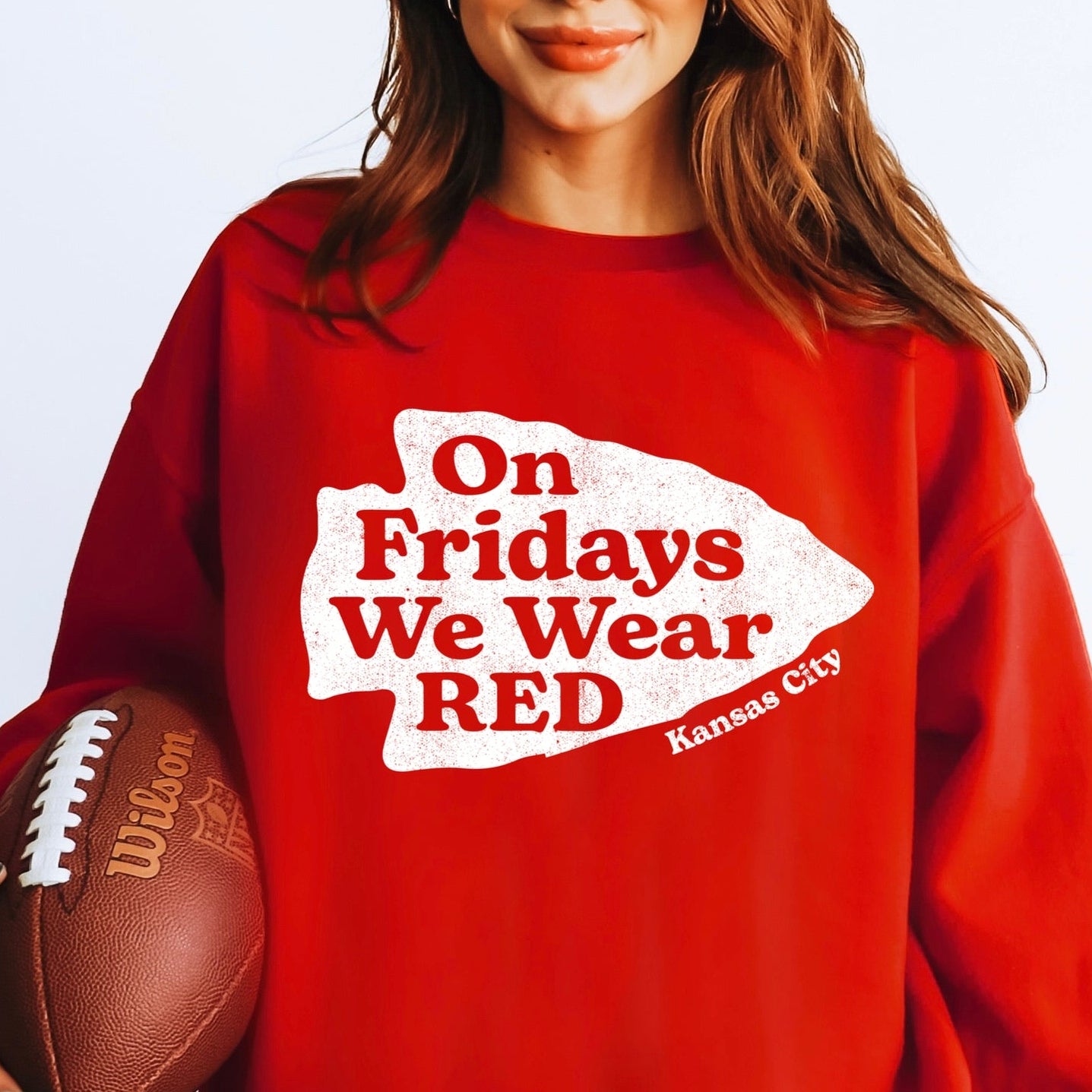 Person wearing a red sweatshirt with 'On Fridays We Wear RED' text, holding a football.