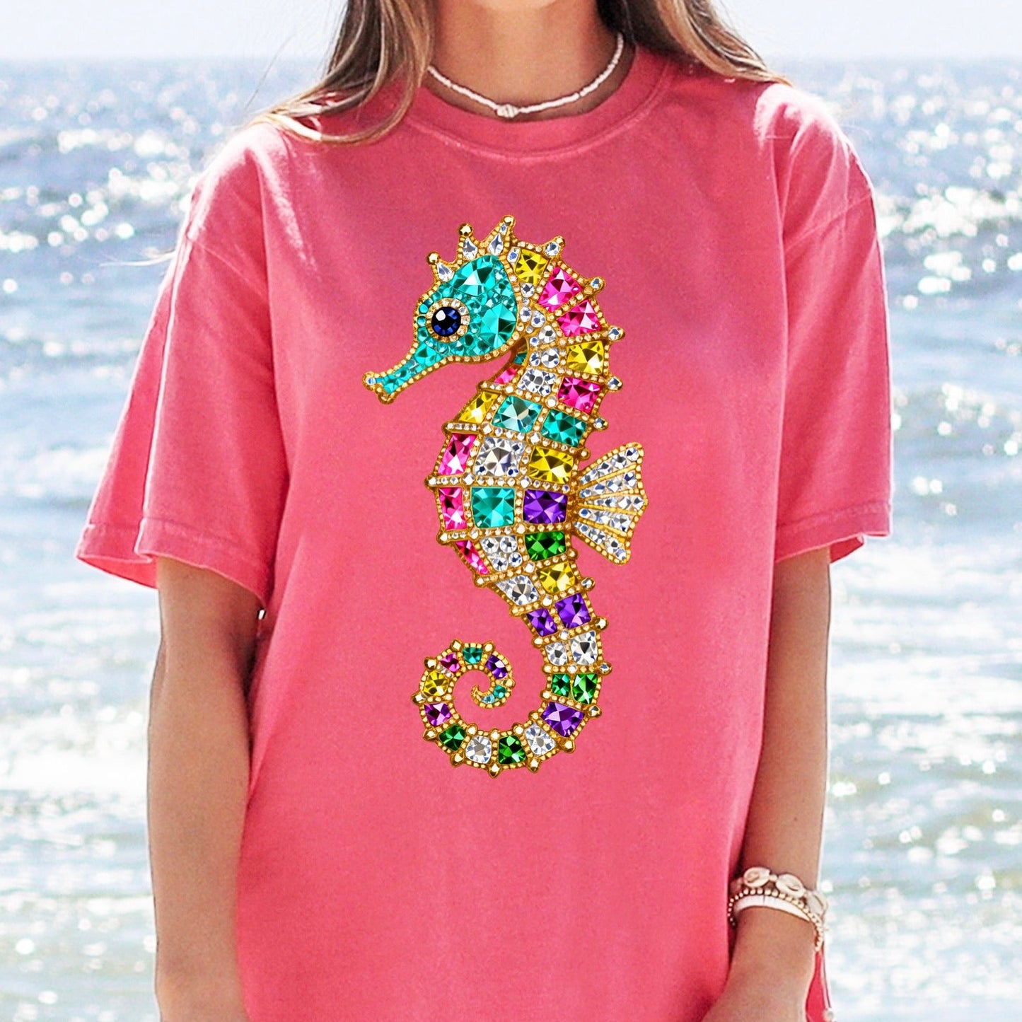 Person wearing a pink t-shirt with a colorful seahorse design on a beach.