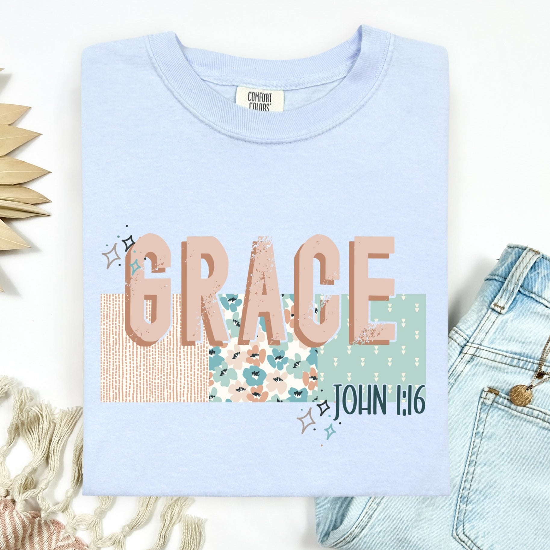 Light blue t-shirt with 'GRACE' and 'John 1:16' text, surrounded by decorative items on a white background