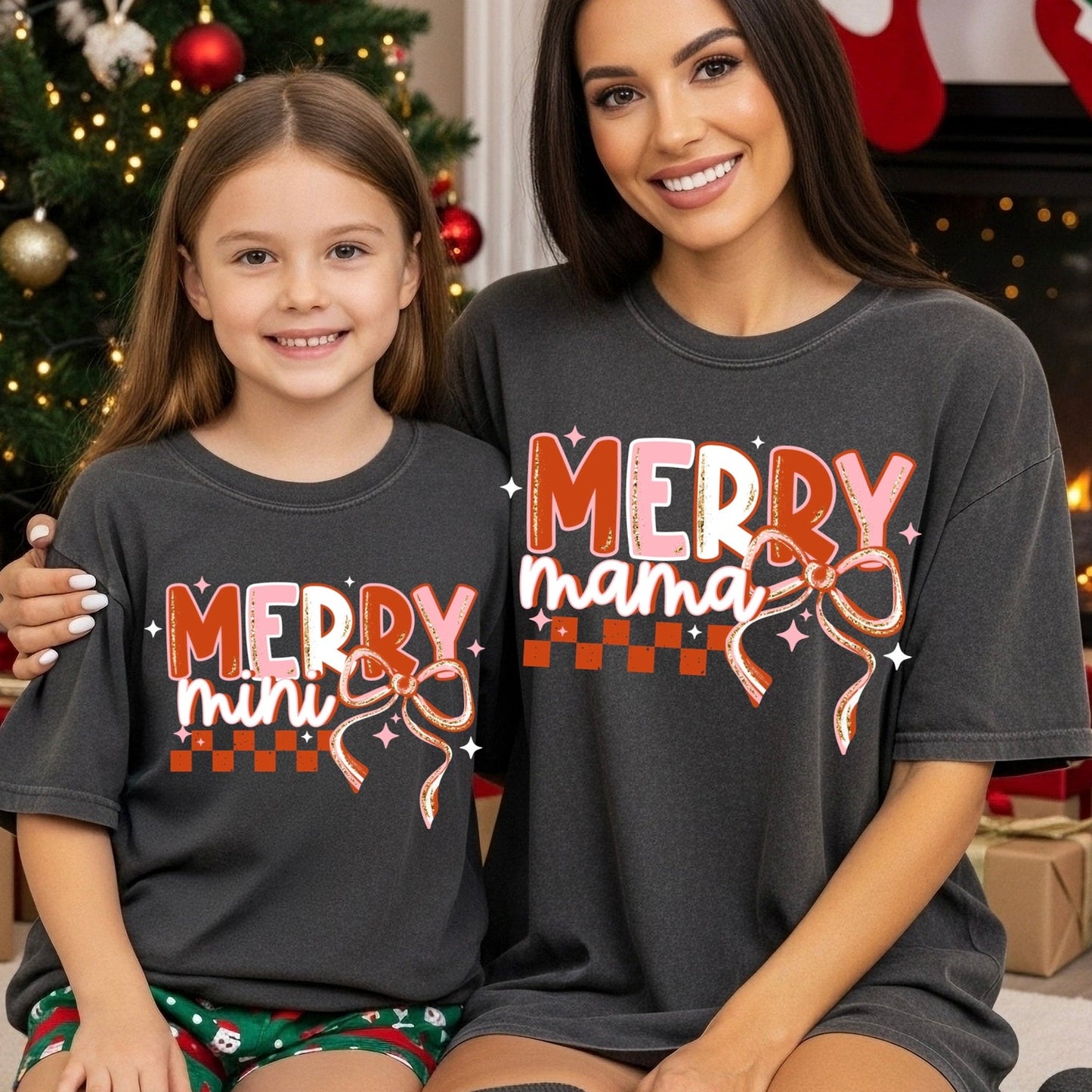 Two people wearing matching 'Merry mini' and 'Merry mama' shirts in a festive setting with a Christmas tree and presents.