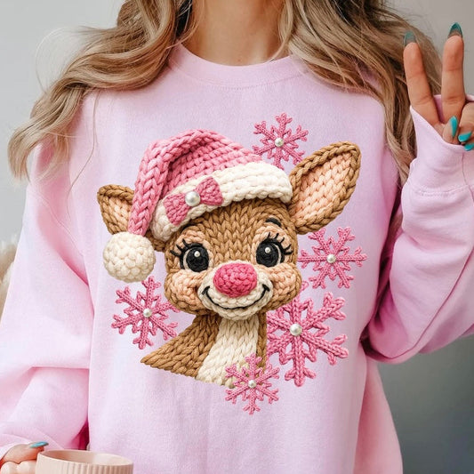 Person wearing a pink sweatshirt with a reindeer design and snowflakes, holding a mug.