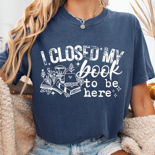 Person wearing a navy blue t-shirt with a book-themed design and text, sitting on a couch.