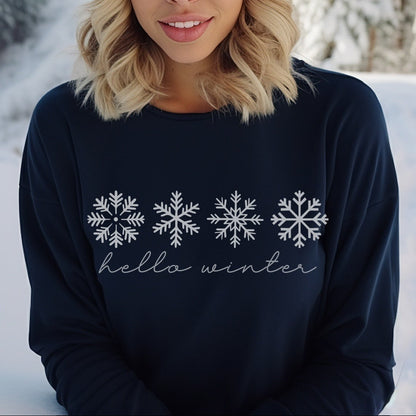 Woman wearing a navy sweater with snowflake designs and 'hello winter' text, standing in a snowy landscape.