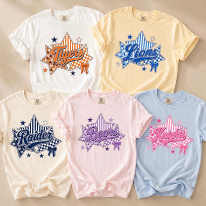 Five short-sleeve graphic T-shirts arranged in a 2x3 flat lay on a light beige background. The shirts are white, pale yellow, cream, light pink, and light blue, each featuring a large star-shaped graphic with a different animal name ('Tigers', 'Lions', 'Roeves', 'Bears', 'Kruelies') in stylized script over checkered and striped patterns.