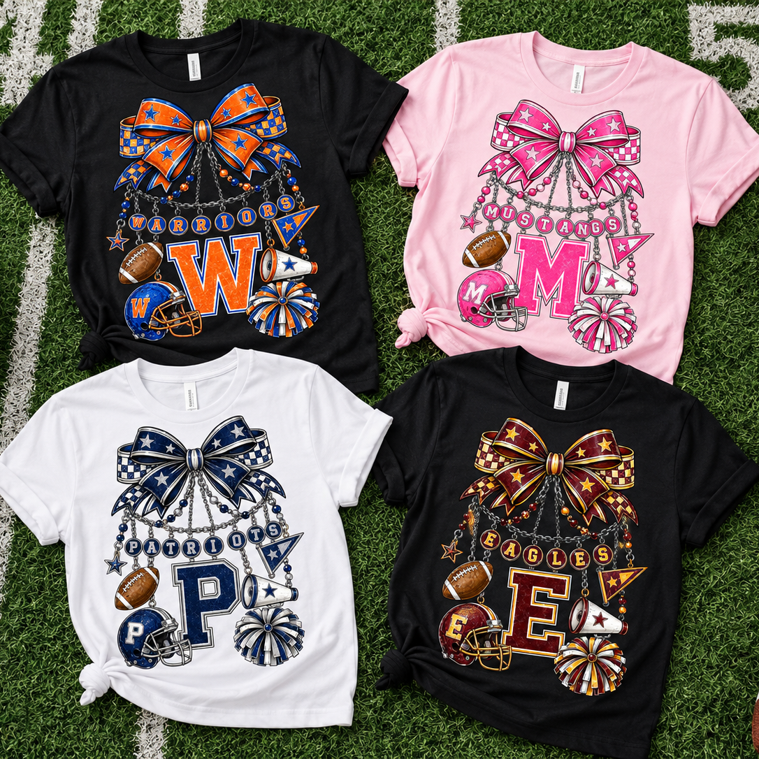 Four short-sleeve graphic T-shirts laid flat on a football-field background with sports props. The shirts are black, pink, and white, each featuring a large decorative bow and cheerleader-themed graphic with monogram letters and football motifs.